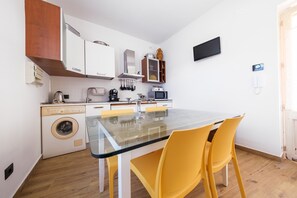 Ett kompakt kök med tvättmaskin, mikrovågsugn och en matplats med ett glasbord och gula stolar.