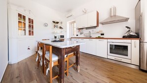 A modern kitchen with white cabinetry, a wooden dining table, and a stainless steel oven. - Apartment 'Vanedda Di Mari - Casa Arancio' with Shared Terrace, Wi-Fi & Air Conditioning (Messina)