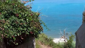 A coastal path with a view of the sea, a stone wall, and greenery. - Apartment 'Vanedda Di Mari - Casa Arancio' with Shared Terrace, Wi-Fi & Air Conditioning (Messina)