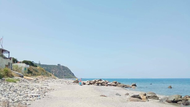 A beach with a rocky shoreline, a person walking, and a building on the left. - Apartment 'Vanedda Di Mari - Casa Arancio' with Shared Terrace, Wi-Fi & Air Conditioning (Messina)