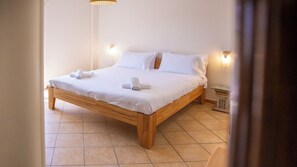 Uma cama de solteiro com roupa de cama e toalhas brancas, estrutura de madeira e duas luzes fixadas na parede.