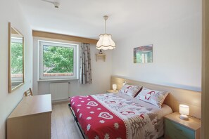 Ein Schlafzimmer mit Bett, Nachttischen, einem Fenster, einem Schreibtisch und einer Pendelleuchte.