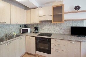 Eine moderne Küche mit hellen Holzschränken, einer Mikrowelle, einer Kaffeemaschine, einem Backofen und einem Flachbildfernseher.