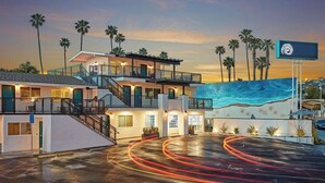 Ein mehrstöckiges Hotel mit Pool, Palmen und einem Sonnenuntergangshimmel.