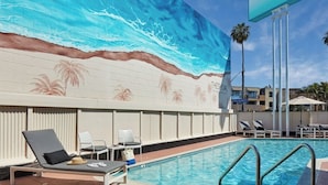 Ein Swimmingpool mit Liegestühlen, ein Wandbild mit Strandmotiv und ein Schild für Theshoal La Jolla.