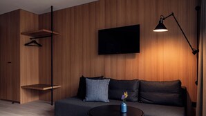 En moderne stue med sofa, ophængt fjernsyn, lampe og et lille bord med en vase.