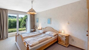 A bedroom with two beds, a window with curtains, a bedside table with a lamp, and a wall-mounted light. - Apartment Tanne – Opposite Ski Lift with Private Terrace, Garden, and Green Views (Schönwald im Schwarzwald)
