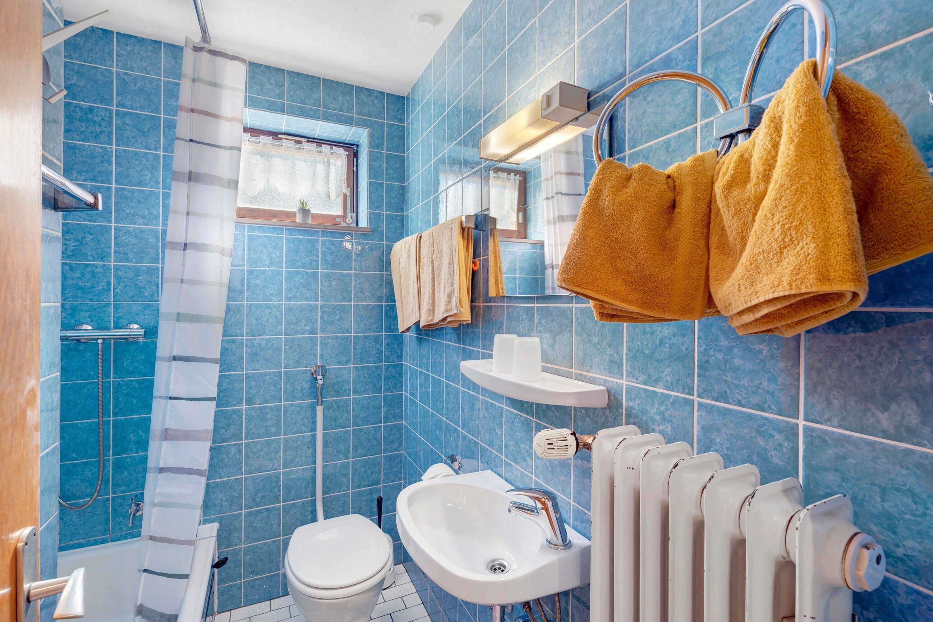 Un baño con azulejos azules, un lavamanos blanco, un inodoro, una ducha y toallas colgadas en un perchero.