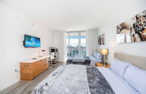 Ein Hotelzimmer mit Bett, Schreibtisch, Fernseher, einem Fenster mit Blick auf die Stadt und Bildern an den Wänden.