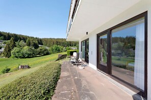 A modern building with large windows, a stone patio, and a view of a green landscape. - Charming Apartment Birke – Opposite Ski Lift with Private Terrace, Garden & Green Views (Schönwald im Schwarzwald)