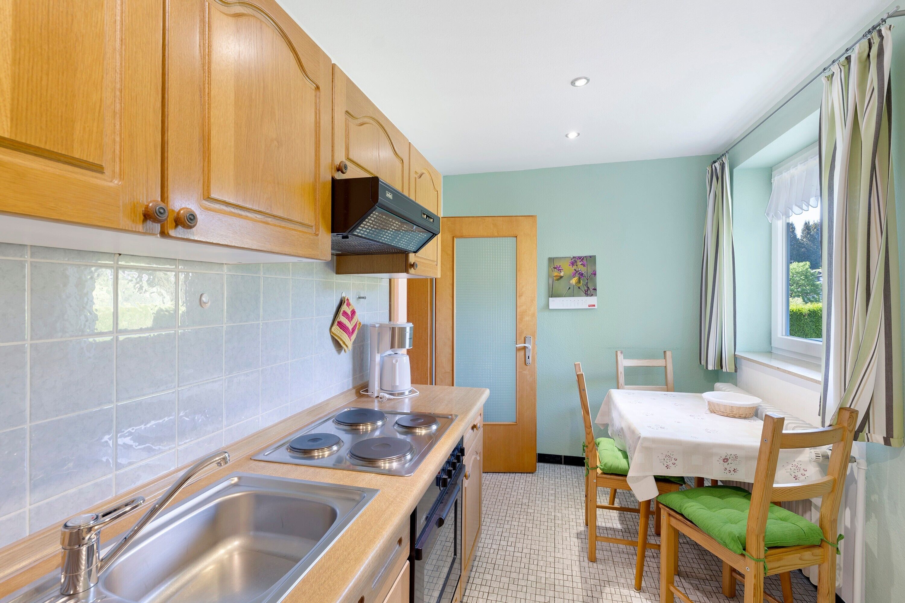 Una cocina con armarios de madera, un lavamanos de acero inoxidable, una estufa y un comedor con mesa y sillas.