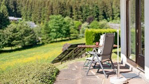 Un patio con mesa y sillas, una terraza de madera y vistas a un área boscosa.