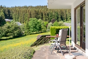 En terrasse med bord og stole, en træterrasse og udsigt til et skovområde.