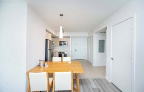Eine moderne Küche mit Edelstahlgeräten, ein Essbereich mit Holztisch und weißen Stühlen sowie ein Flur, der zu einer Tür führt.