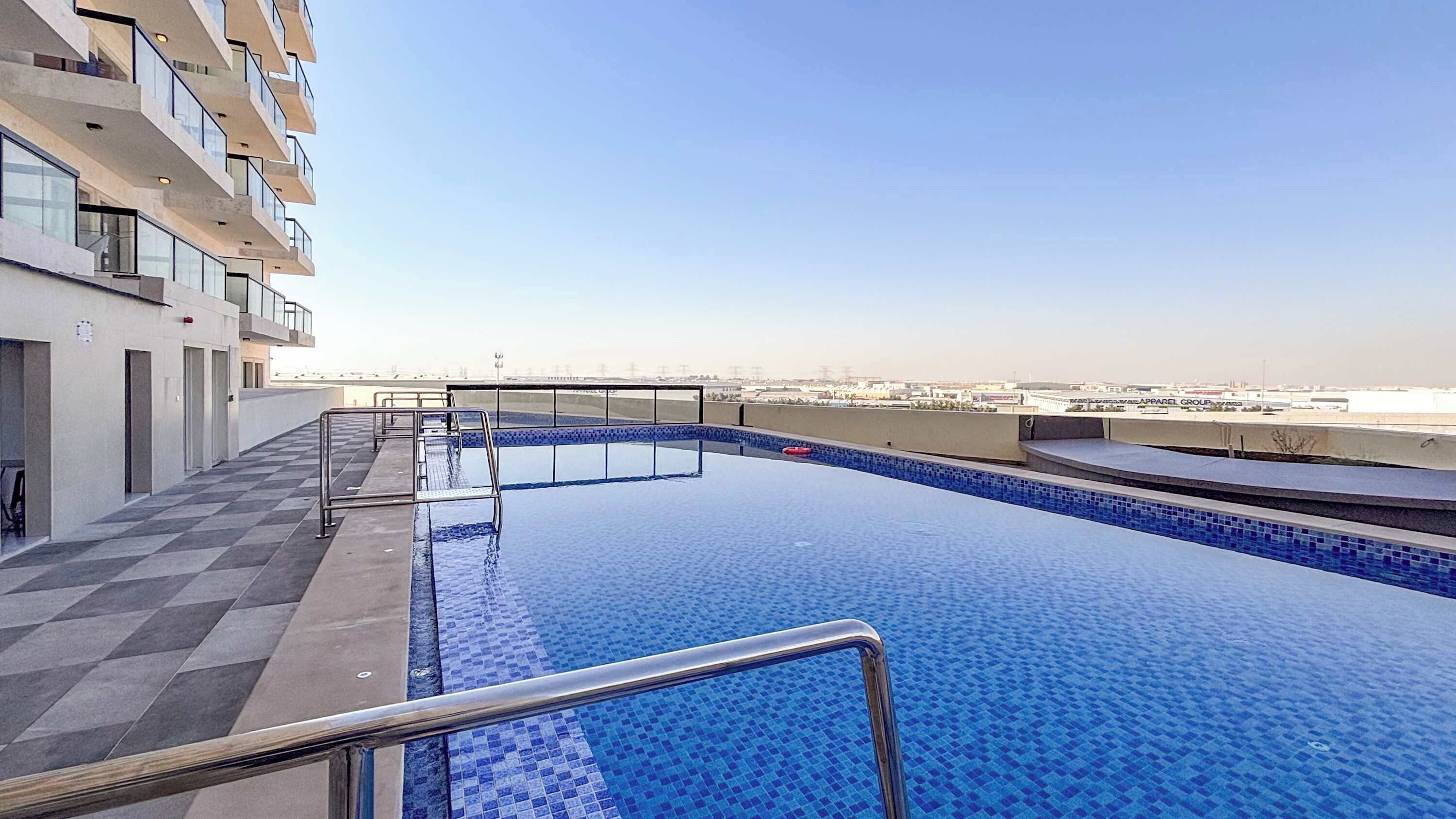A rooftop pool with clear blue water, surrounded by a checkered floor, and a view of the cityscape in the background.