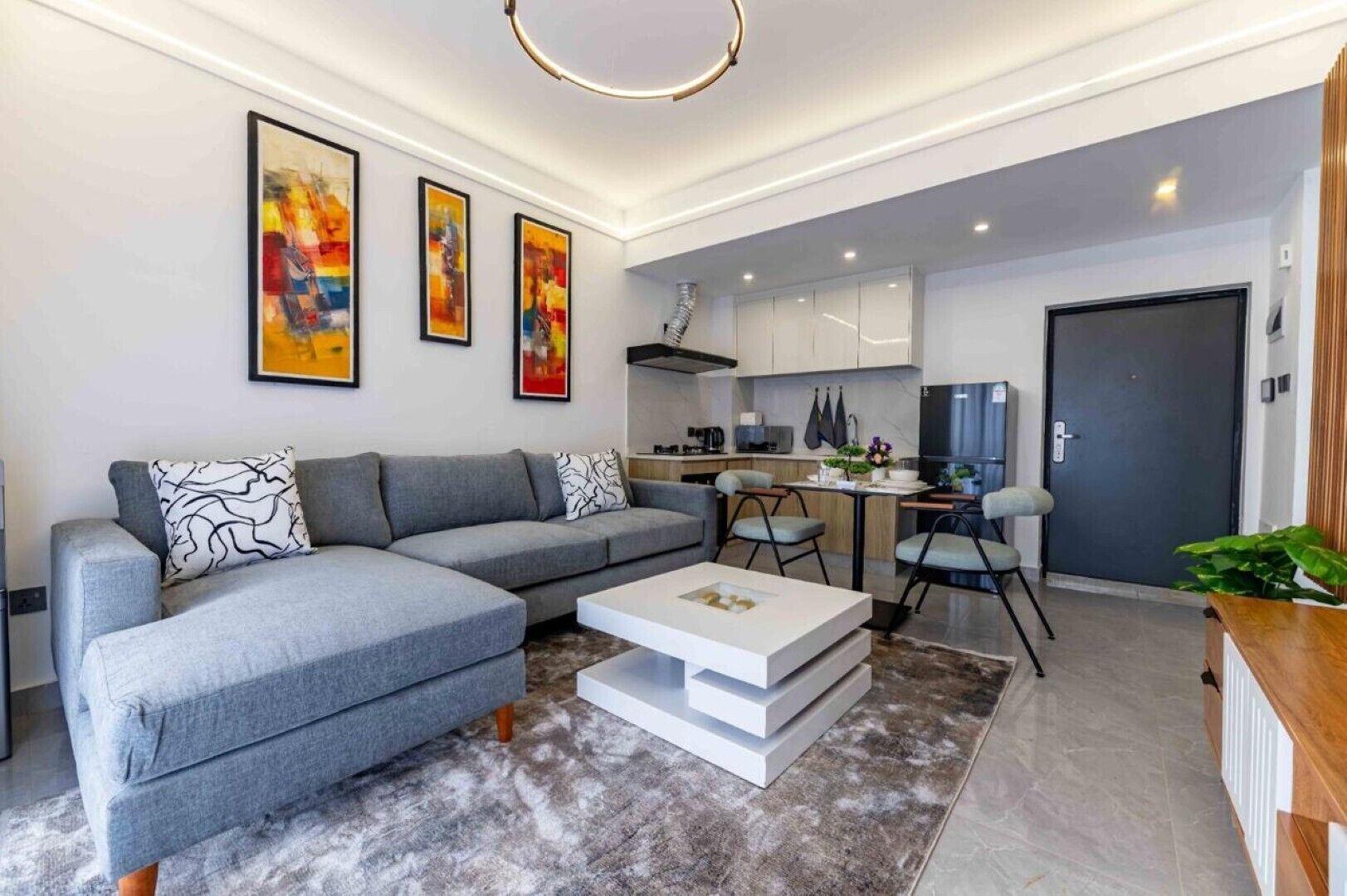A modern living room with a grey sectional sofa, a white coffee table, and a kitchen area with a dining table and chairs.