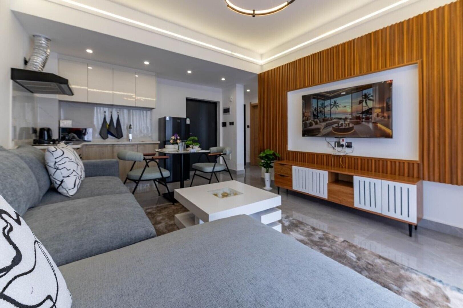 A modern living room with a grey sofa, a coffee table, and a TV mounted on a wooden wall.