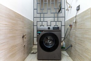 Ein kompakter, moderner Waschraum mit einer Waschmaschine mit Frontlader, einem Metallgestell und einem Warmwasserbereiter.