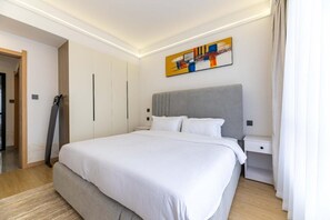 Ein modernes Hotelzimmer mit einem großen Bett, einem grauen Kopfteil, einem Nachttisch, einem Kleiderschrank und einem farbenfrohen abstrakten Gemälde an der Wand.