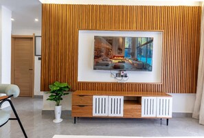 Ein modernes Wohnzimmer mit großem Fernseher an einer Holzwand, einer weißen Unterhaltungseinheit und einer Topfpflanze.