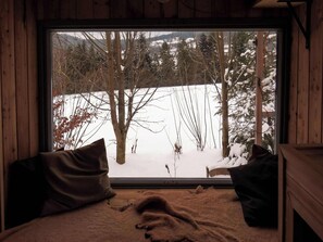 A room with a large window, a bed with a blanket, and two pillows.