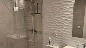 Een moderne badkamer met een douche met glazen wand, een toilet en een wastafel met spiegel.