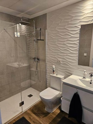 Ein modernes Badezimmer mit einer Duschkabine, einer Toilette und einem Waschbecken mit Spiegel.