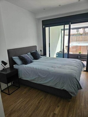 Ein modernes Schlafzimmer mit einem großen Bett, einem Nachttisch und einer Schiebetür zu einem Außenbereich.