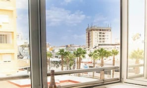 A view from a window overlooking a cityscape with palm trees, buildings, and a clear sky. - Amazonia – Downtown Torremolinos – Quiet Apartment for 4 Gue (Torremolinos)
