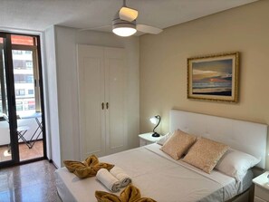 Ein Hotelzimmer mit Bett, Nachttisch, Deckenventilator, einem Gemälde und einer Schiebetür zum Balkon.