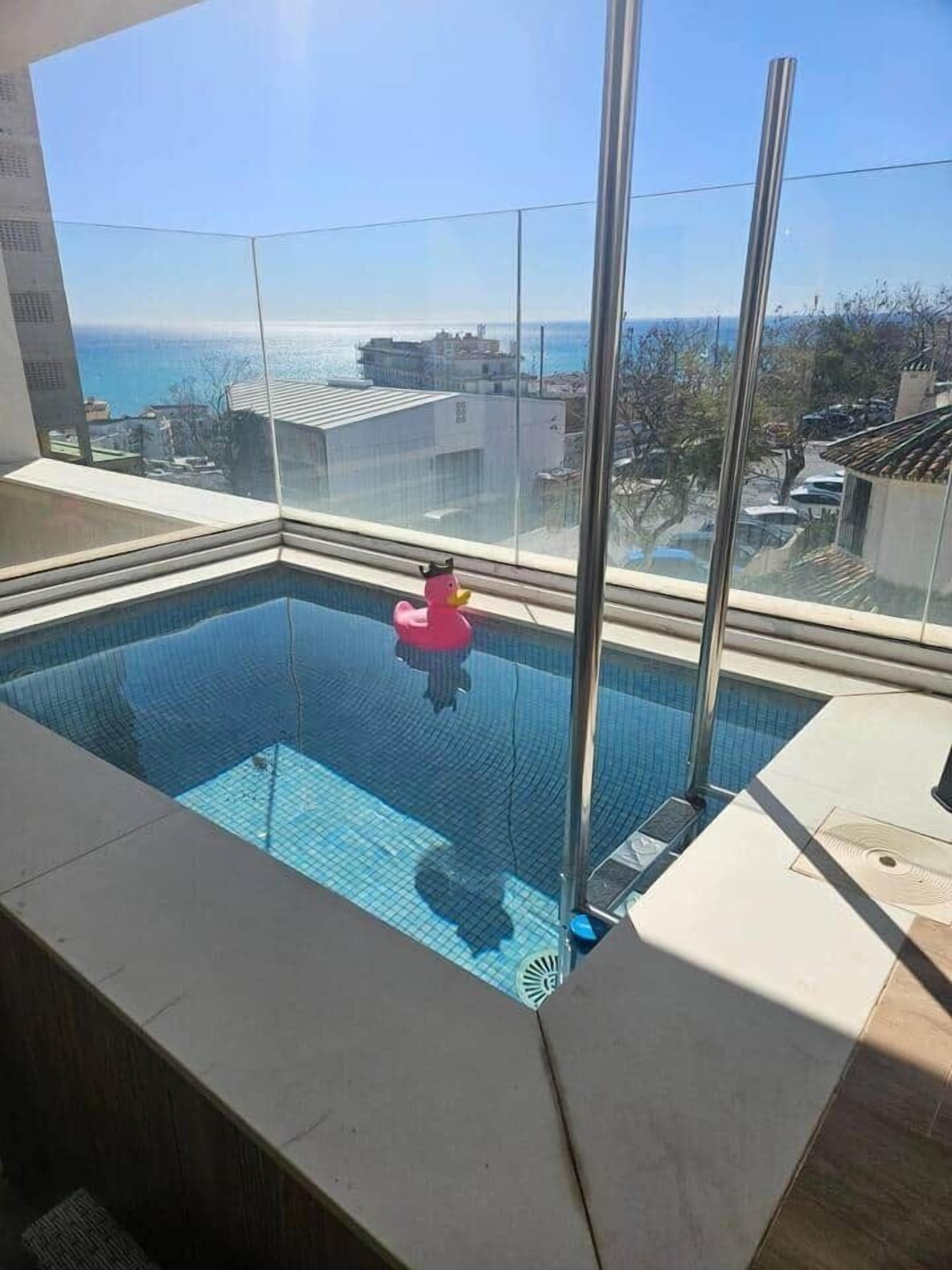 Ein Pool auf dem Dach mit Blick aufs Meer, eine rosa Quietscheente und eine Glasumrandung.