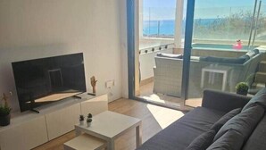 Un soggiorno moderno con una TV a schermo piatto, un divano, un tavolino da caffè e un balcone con vista mare.