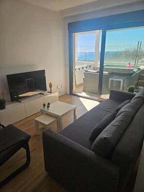 A modern living room with a flat-screen TV, a sofa, a coffee table, and a balcony with a view of the sea. - Horizon Del Mar – Sea Views & Plunge Pool – 2BR, 2BA, Sleeps (Torremolinos)