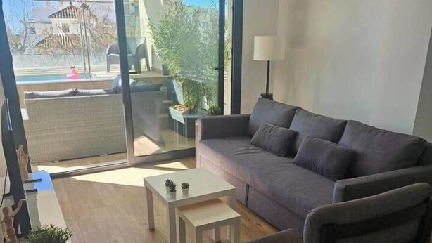 Un soggiorno moderno con divano, poltrona, tavolino e vista su una zona esterna tramite una porta in vetro.