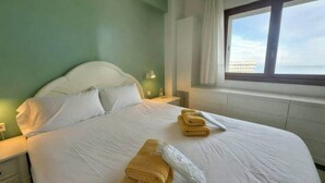 Quarto de hotel com cama, duas mesinhas de cabeceira, janela com vista e toalhas na cama.