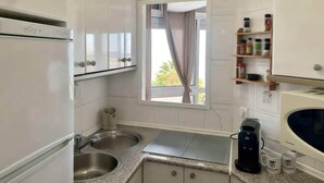 Uma cozinha compacta com micro-ondas, cafeteira e janela com cortinas.
