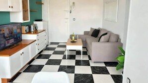 Uma sala de estar com chão xadrez, um sofá, uma mesa de centro e uma televisão sobre um móvel.