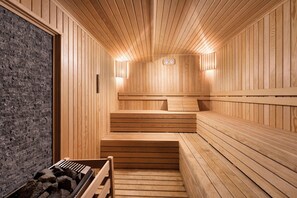 Una sauna con paredes y bancos de madera, una pared de piedra en un lateral, y dos luces fijadas a la pared.