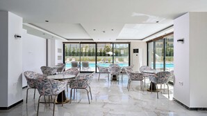 Un espace intérieur moderne avec vue sur la piscine, agrémenté de chaises et de tables aux motifs originaux, et doté d’un mur en verre.