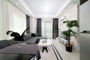 A modern living room with a sofa, a coffee table, a TV, and a potted plant. - Annabella Residence (Alanya)
