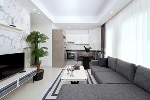 A modern living room with a flat-screen TV, a grey sofa, a coffee table, and a potted plant. - Annabella Residence (Alanya)