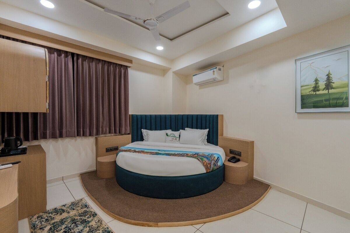 Un dormitorio con cama, un escritorio, una silla, una ventana con cortinas, un equipo de aire acondicionado y un cuadro en la pared.