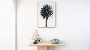 A framed palm tree artwork on a wall, a small sailboat model on a wooden table, and a bowl of pebbles. - Spacious Ocean View Unit — Pool, Tennis & Beaches (Surfers Paradise)
