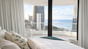 A bedroom with a balcony, white bedding, and a view of the ocean and buildings. - Spacious Ocean View Unit — Pool, Tennis & Beaches (Surfers Paradise)