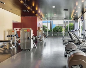 Ein Fitnessraum mit Cardiogeräten, Gewichten und großen Fenstern mit Blick ins Freie.