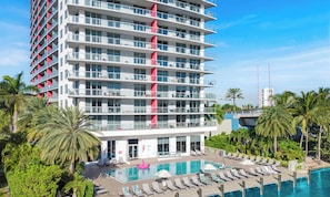 A multi-story hotel with a pool area, palm trees, and a clear sky. - Hallandale Studio | Pool, Gym & Shuttle (Hallandale Beach)