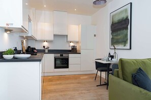 A modern kitchen with white cabinets, a black countertop, and a dining area with a green sofa. - Desirable one bedroom apartment (Southampton)