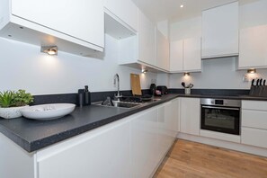 A modern kitchen with white cabinets, a black countertop, and built-in appliances including a stove and oven. - Desirable one bedroom apartment (Southampton)