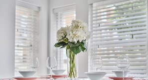 A dining table with a vase of white flowers, white plates, and wine glasses. - Stylish Windsor Stay | Steps from The Long Walk | Private Parking (Windsor)