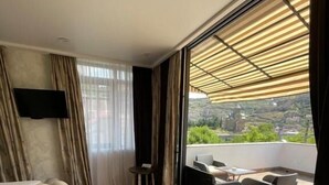 Quarto com uma cama grande, televisão fixada na parede e varanda com mobiliário de exterior.